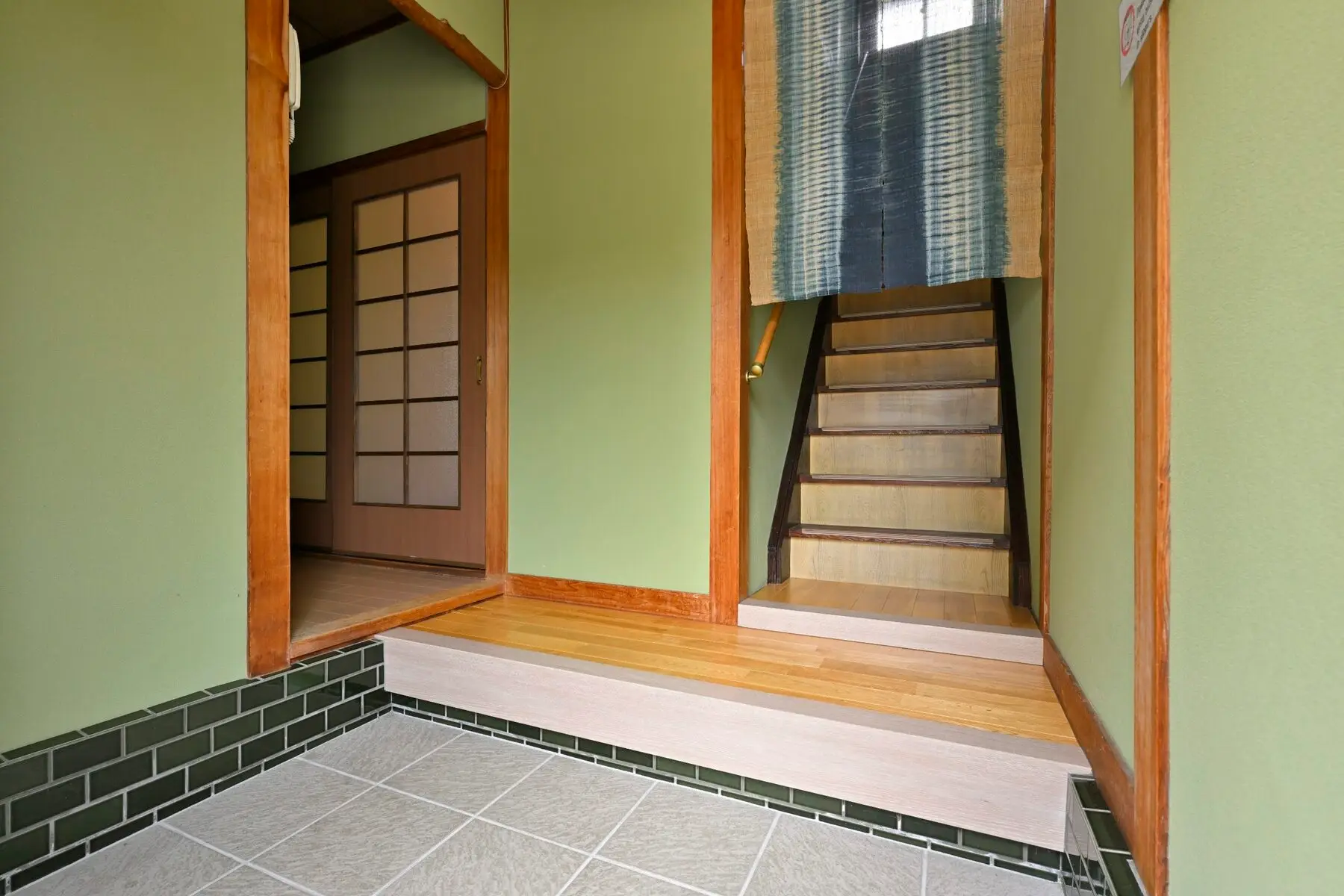 玄関 — 緑の壁。上がり框に腰かけて靴を脱ぐ。